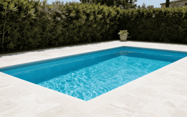 Balcon de piscine extérieure avec eau bleue claire, entourée de dalles en pierre naturelle, dans un jardin paysager avec haies vertes.